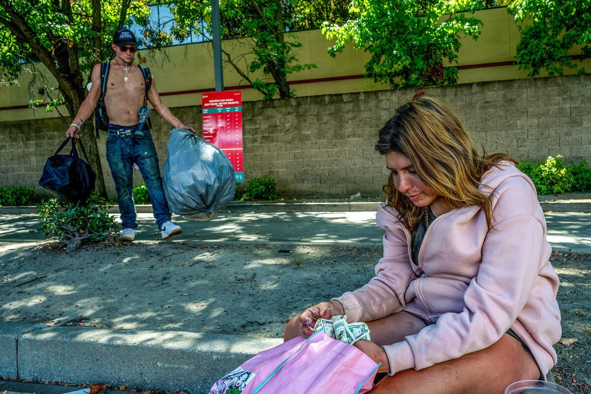 Justin Hartung, 39, carries clothing and other belongings as his girlfriend, Califia Carlisle, counts money collected from drivers at Howe Avenue and Folsom Boulevard in Sacramento in July.